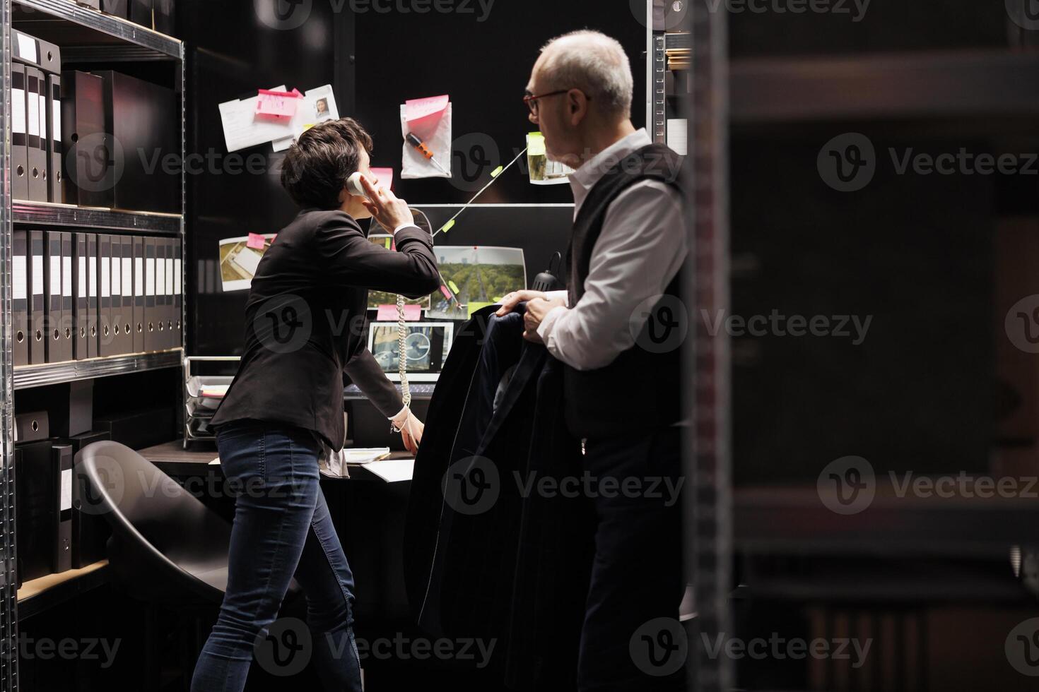 Woman inspector talking with remote police officer about crime scene evidence, working late at night at criminal case in arhive room. Private detectives discussing confidential information photo