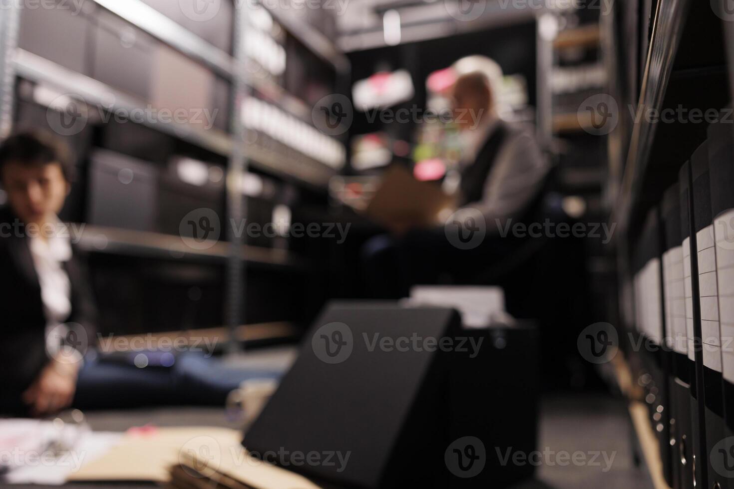 Selectiv focus of storage full with investigation evidence files, in background criminology team analyzing crime scene report. Private detectives working overtime at federal case in arhive room photo