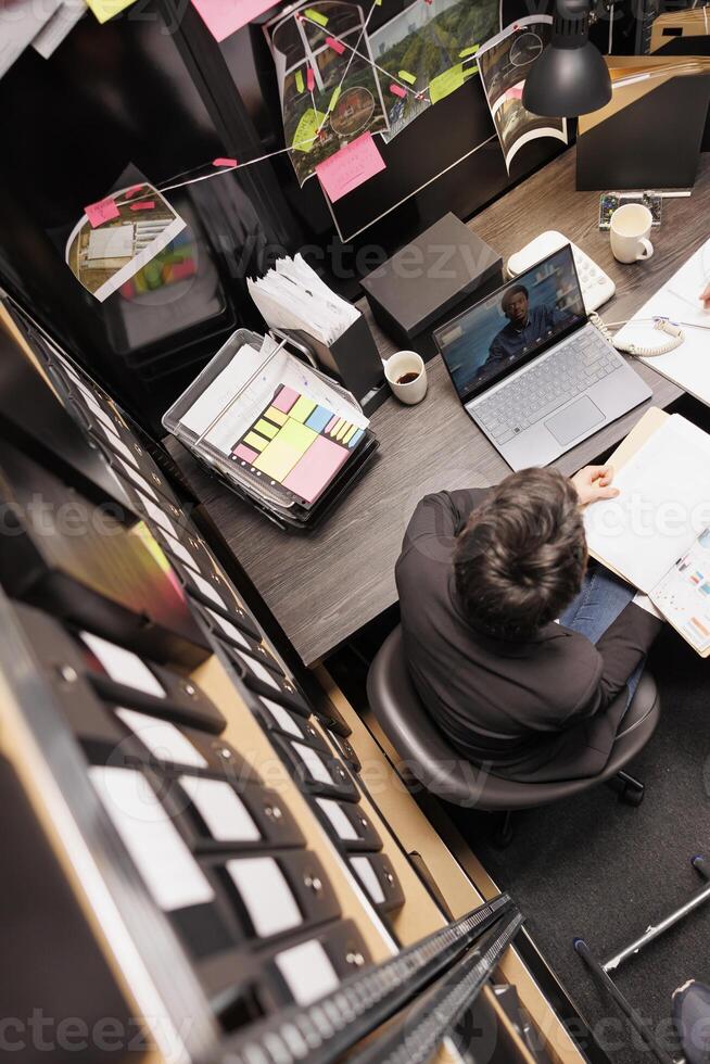 Top view of police officer discussing with remote inspector during online videocall meeting conference on laptop computer. Private detectives working overtime at criminal case in arhive room photo