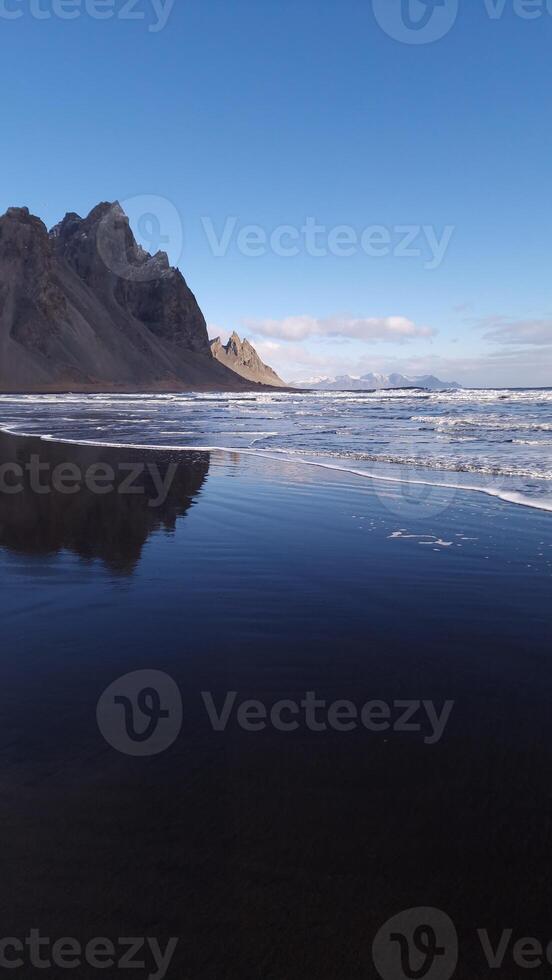 Massive vestrahorn mountains connect with ocean, fantastic nordic setting with unique black sand beach. Icelandic stokksnes peninsula with huge cliffs and hills, breathtaking scenic route. photo
