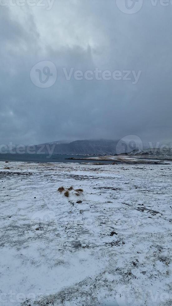 invernal paisaje con escarchado campos en islandés región, masivo Nevado montañas cumbres y congelado tierras invierno mundo maravilloso borde del camino paisaje con tierras altas y sierras. foto