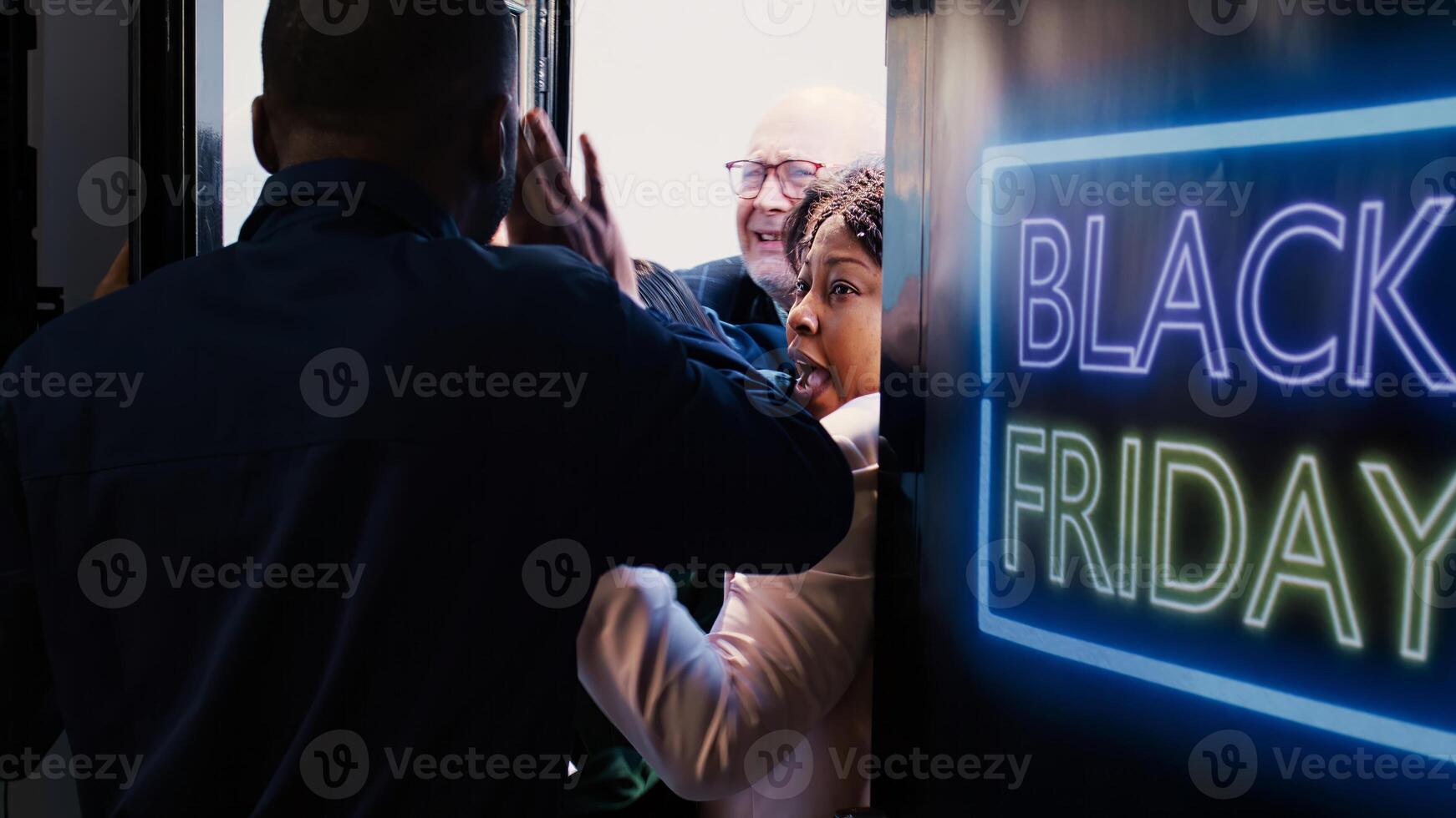 Customers shoving each other out of way to enter store first during black friday shopping spree. African american security agent holding back crazy shoppers breaking inside shopping center. photo