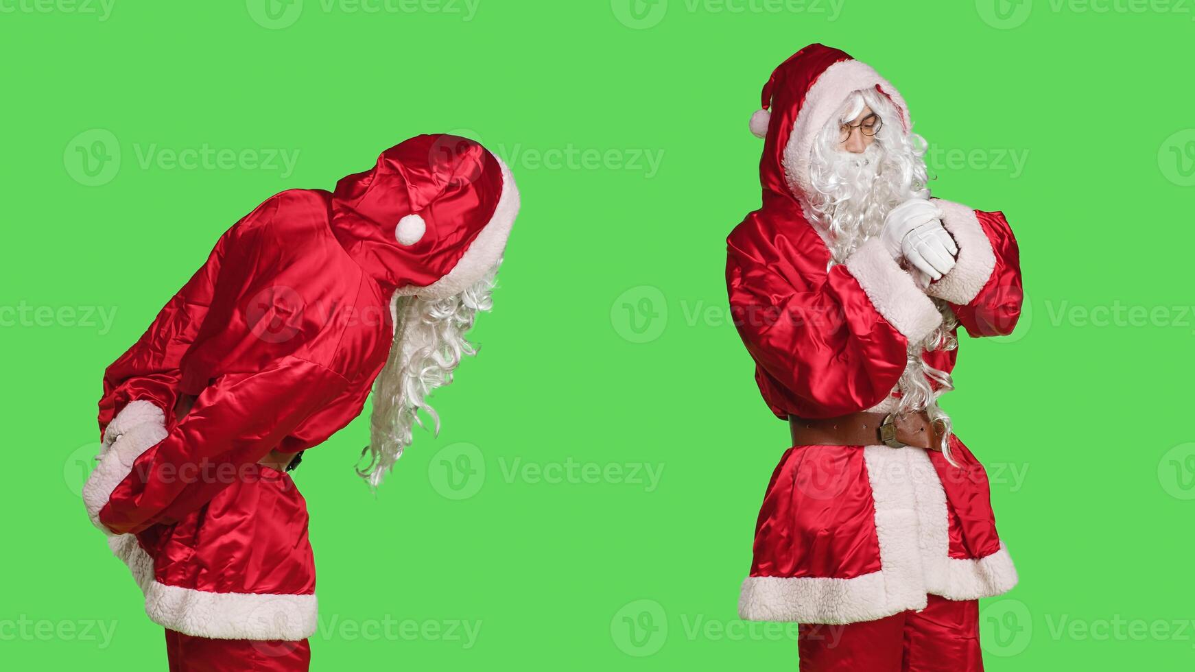 Man in red suit checks wristwatch to see time, posing over greenscreen backdrop. Confident person wearing santa claus festive costume to spread christmas spirit, celebrate winter holiday. photo