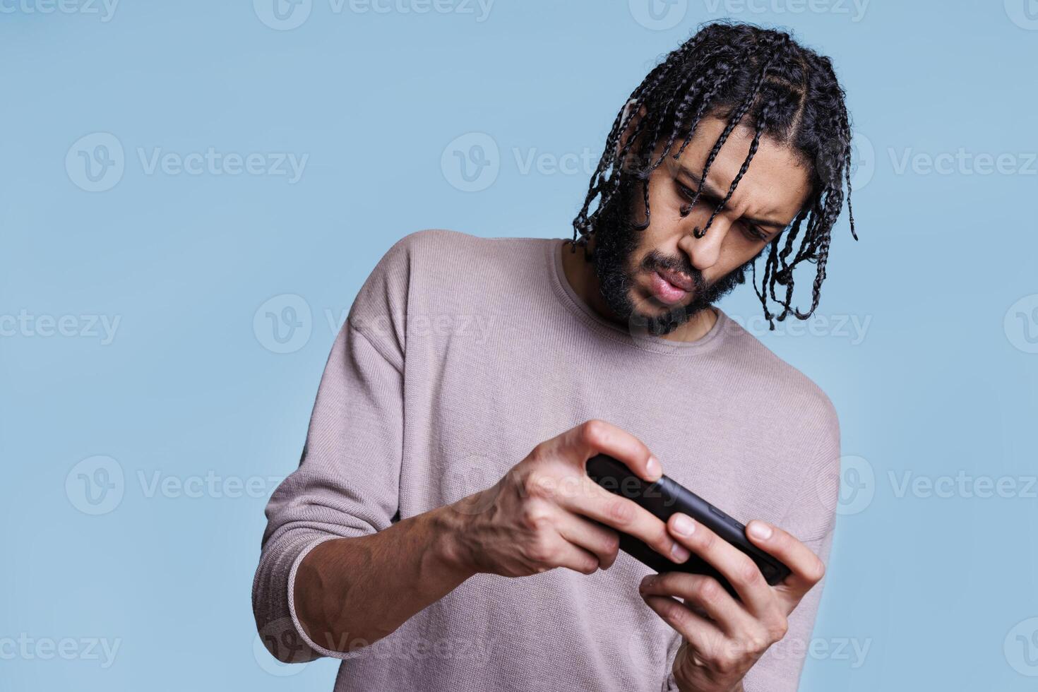Concentrated arab man gamer playing online game on smartphone. Young person holding phone and using entertaining mobile application software with focused facial expression photo