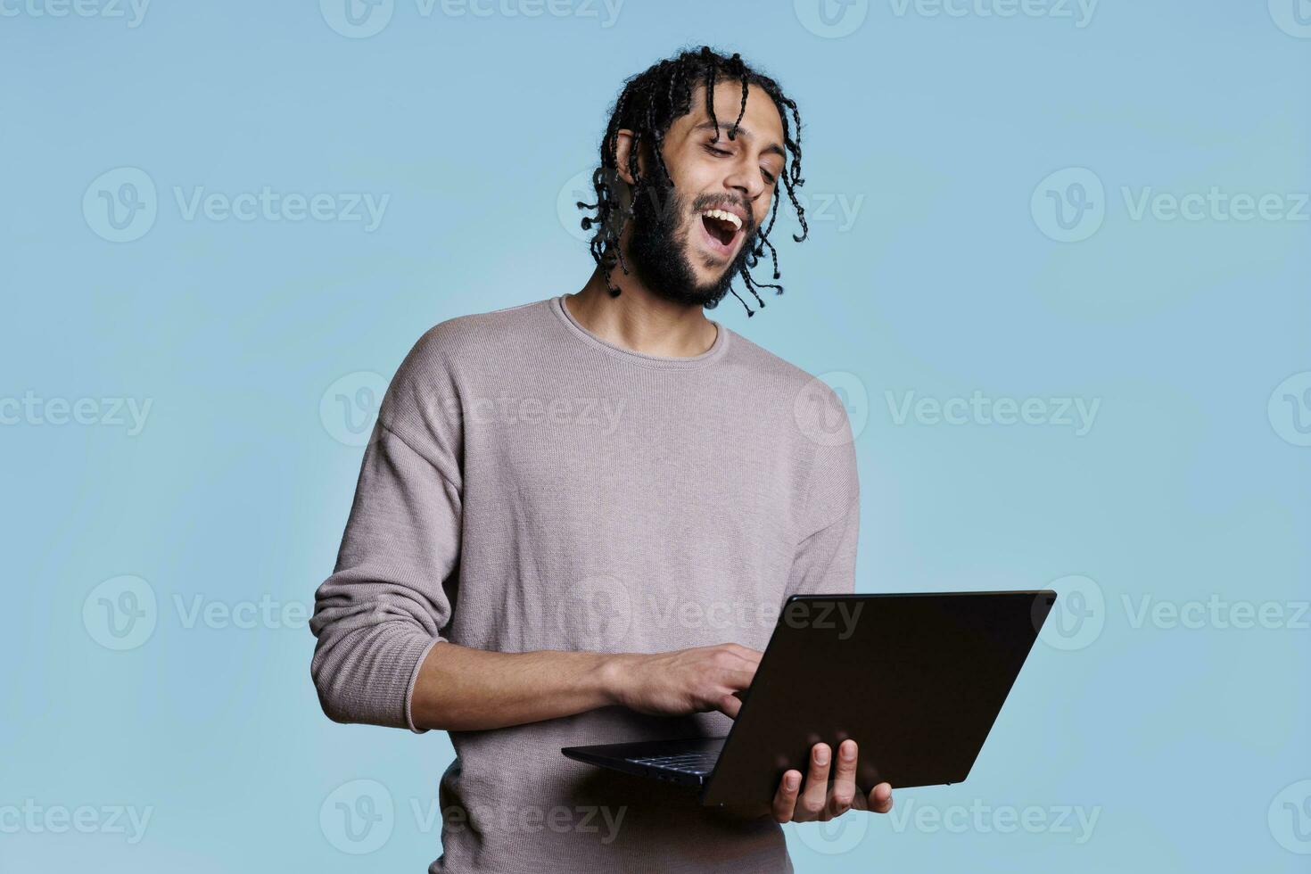 Happy arab man holding laptop and having fun communication in video call. Smiling person with cheerful facial expression holding portable computer and talking in online meeting photo