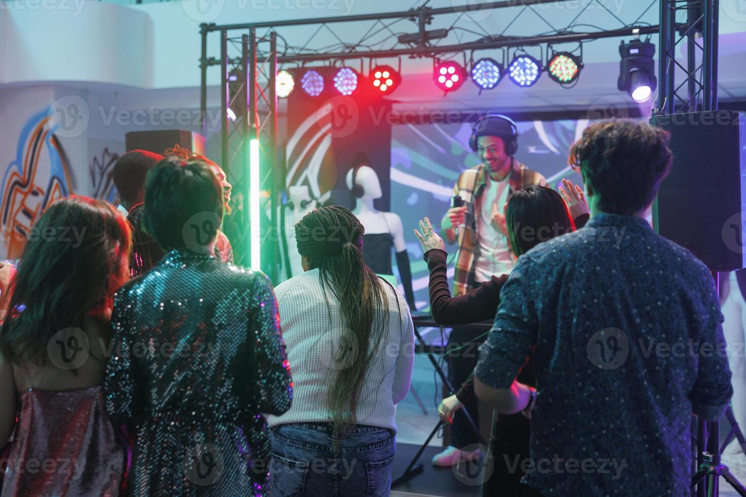 personas bailando y ir de fiesta en Club nocturno mientras joven hombre DJ ejecutando en etapa iluminado con focos multitud clubbing y Moviente en pista de baile a electrónico música concierto foto