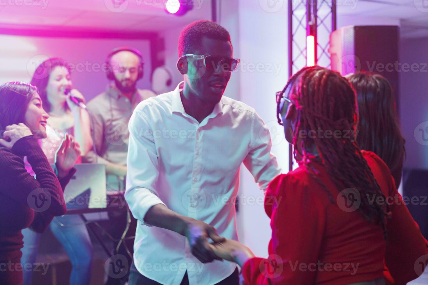 Couple partying on dancefloor in nightclub at discotheque and enjoying nightlife entertainment. African american man and woman dancing while attending electronic music performance photo