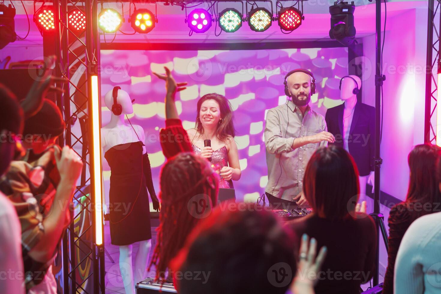 Man and woman musicians playing and singing on stage at electronic music festival in nightclub. Singer and dj techno band performing while people dancing on dancefloor in club photo