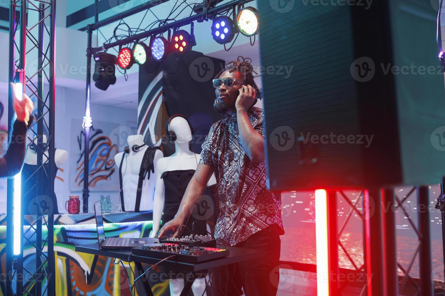 Dj in headphones mixing sounds using digital electronic music controller on stage in nightclub. Young african american man musician performing at discotheque party in club photo