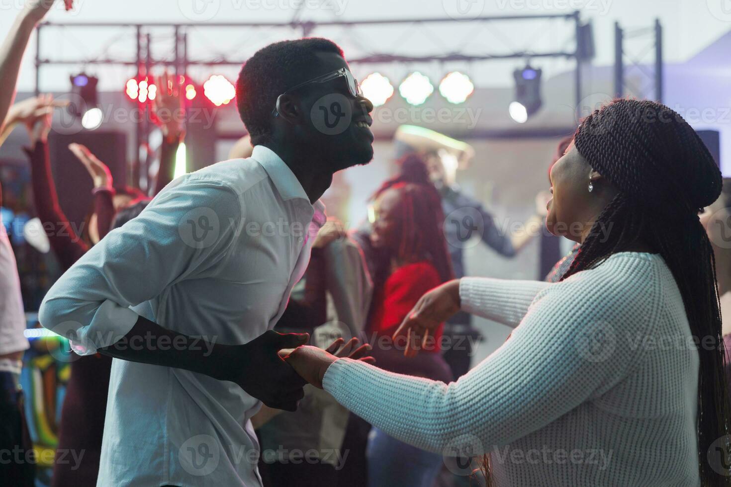 despreocupado africano americano Pareja bailando juntos y teniendo divertido en Club nocturno. alegre joven hombre y mujer clubbers participación manos y ir de fiesta en pista de baile mientras clubbing foto