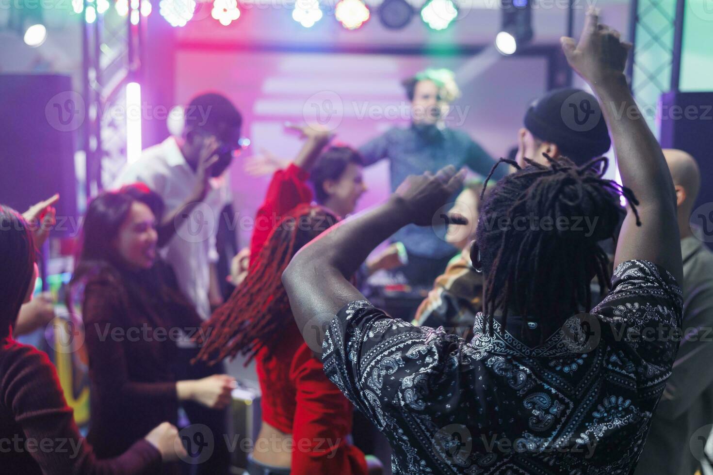 Diverse people dancing and raising hands at discotheque with live music in nightclub. Young clubbers partying, moving to electronic music rhythm and jumping on club dancefloor photo