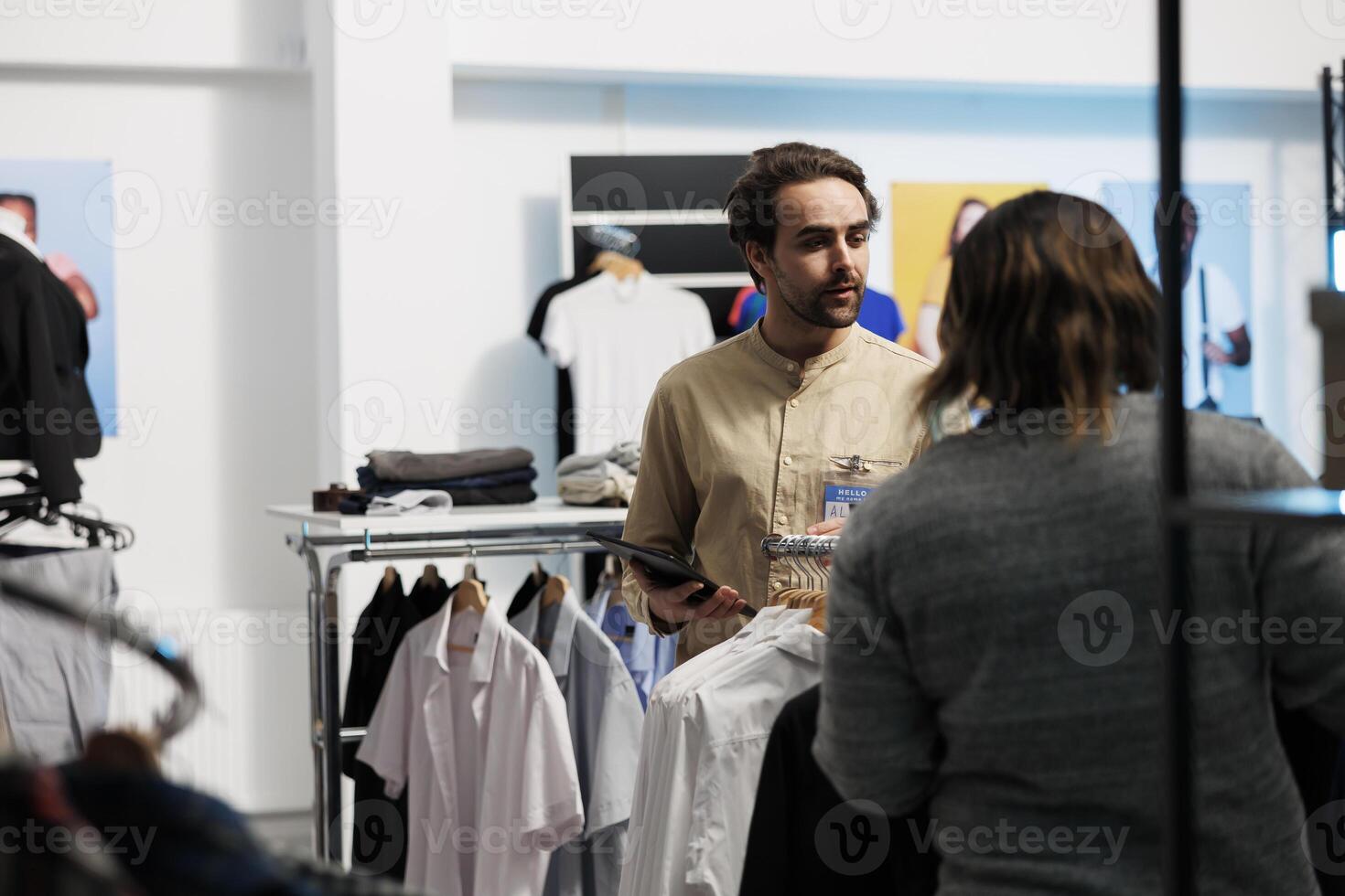 Mall worker standing near clothes rack and checking apparel available for purchase using digital tablet. Shopping center young man employee checking store app on portable gadget photo