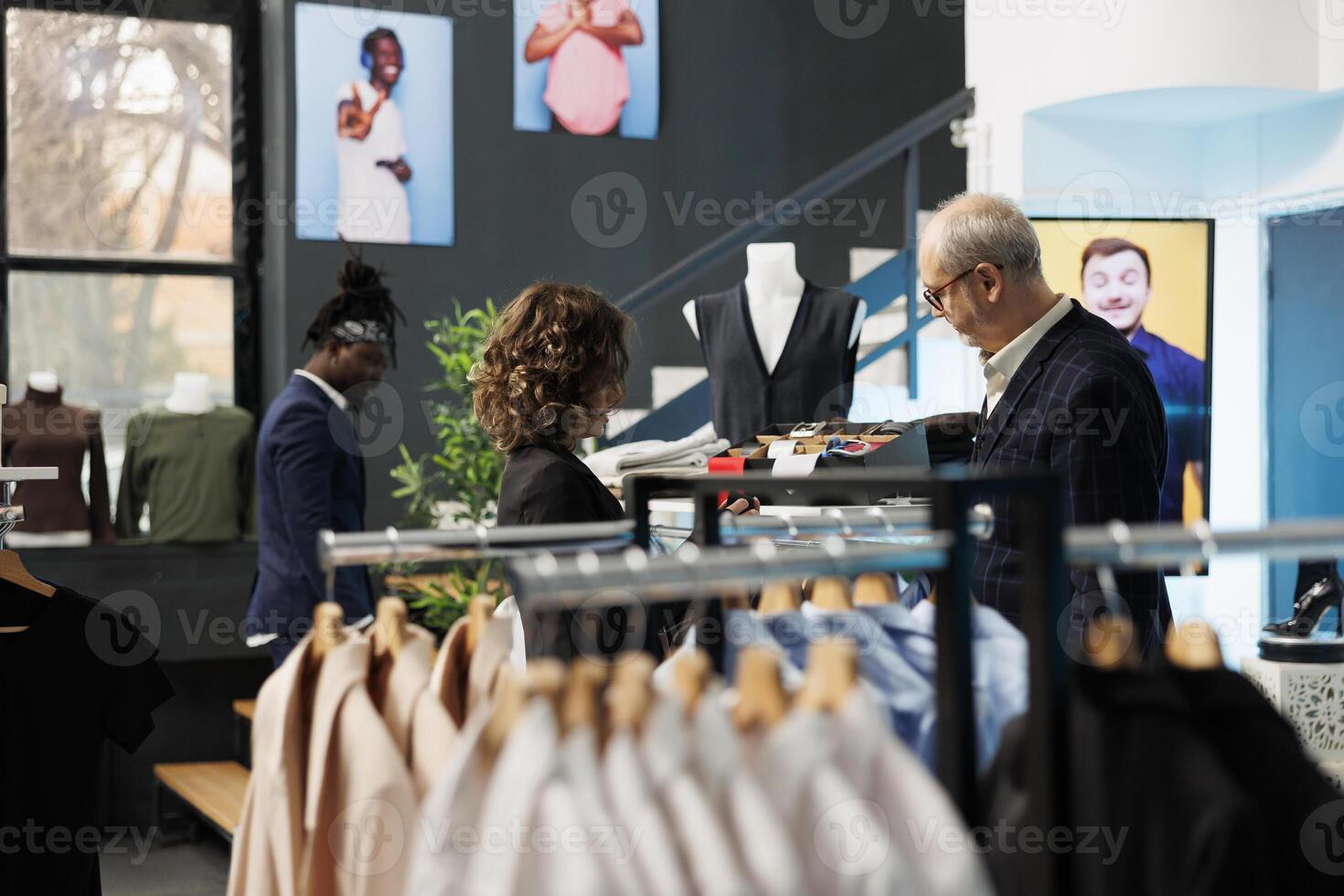 Senior man asking showroom worker for help with tie, customer shopping for formal wear in modern boutique. Elderly client buying fashionable clothes and stylish accessories. Fashion concept photo