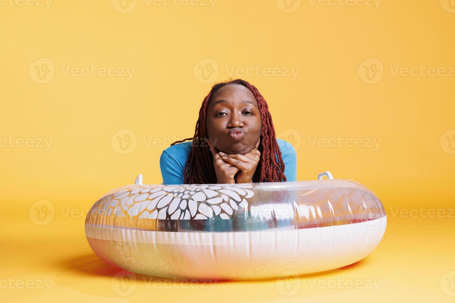 Happy person sitting on inflatable ring, having fun on the floor in studio. Young woman smiling and acting silly on camera with float ring, joyful excited female model laying down. photo