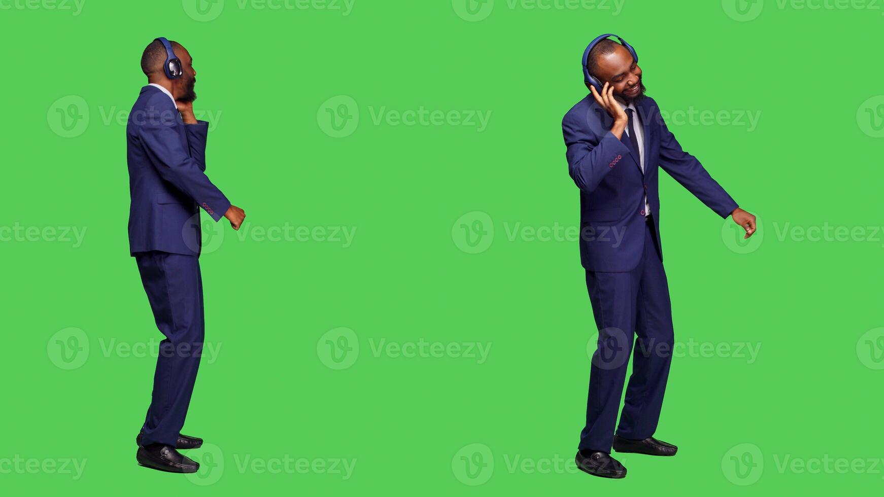 Company employee listening to music and dancing, wearing office suit and audio headset in studio. Young businessman having fun with songs and headphones over green screen backdrop. photo