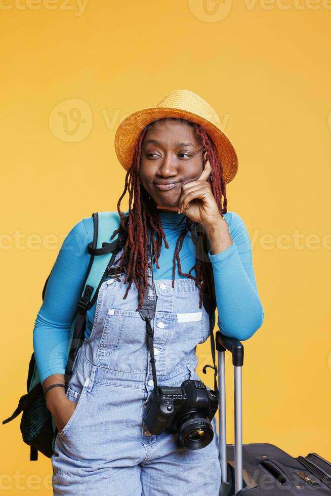 africano americano mujer de viaje en el extranjero, posando en estudio con dslr cámara y carretilla bolsas. hembra viajero yendo en internacional Aléjate para fin de semana actividades, urbano destino. foto