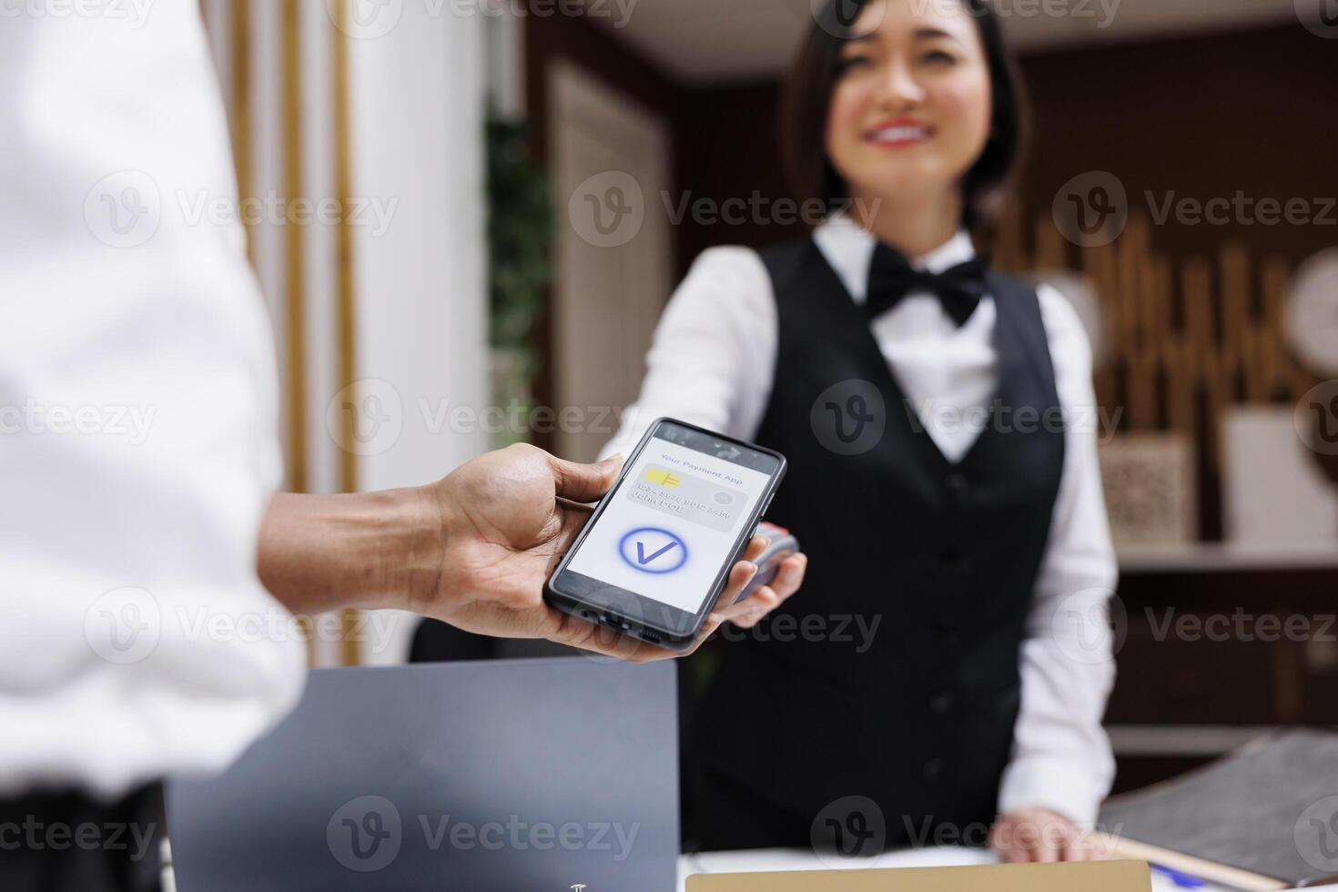 African american man using phone nfc to pay for room booking at reception counter, front desk. Young guest paying on pos terminal, electronic payment at check in registration. Close up. photo