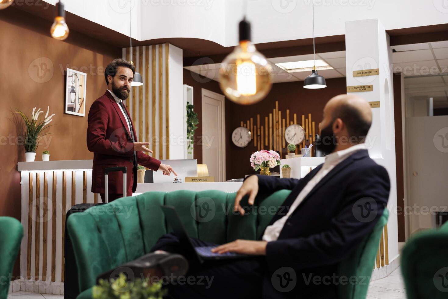 Businessmen talking about hotel service, asking where the receptionist is. Guest traveller ringing service bell to call for concierge and help with check in procedure, man on business trip. photo