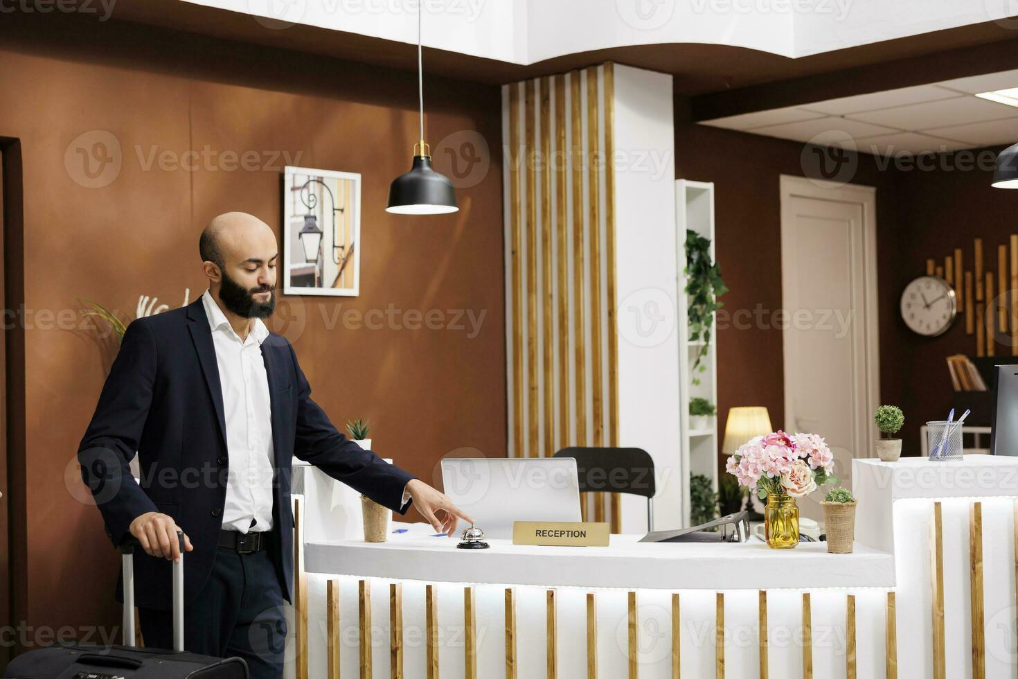 Businessman at hotel front desk using service bell to ring for concierge assistance, preparing for room registration. Entrepreneur checking in at resort, corporate business conference. photo