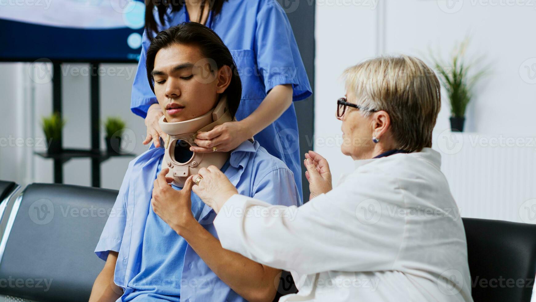 Traumatologist helping asian patient to take of cervical neck collar in hospital waiting room, explaining medical treatment. Elderly medic receiving medicine support during checkup visit appointment photo