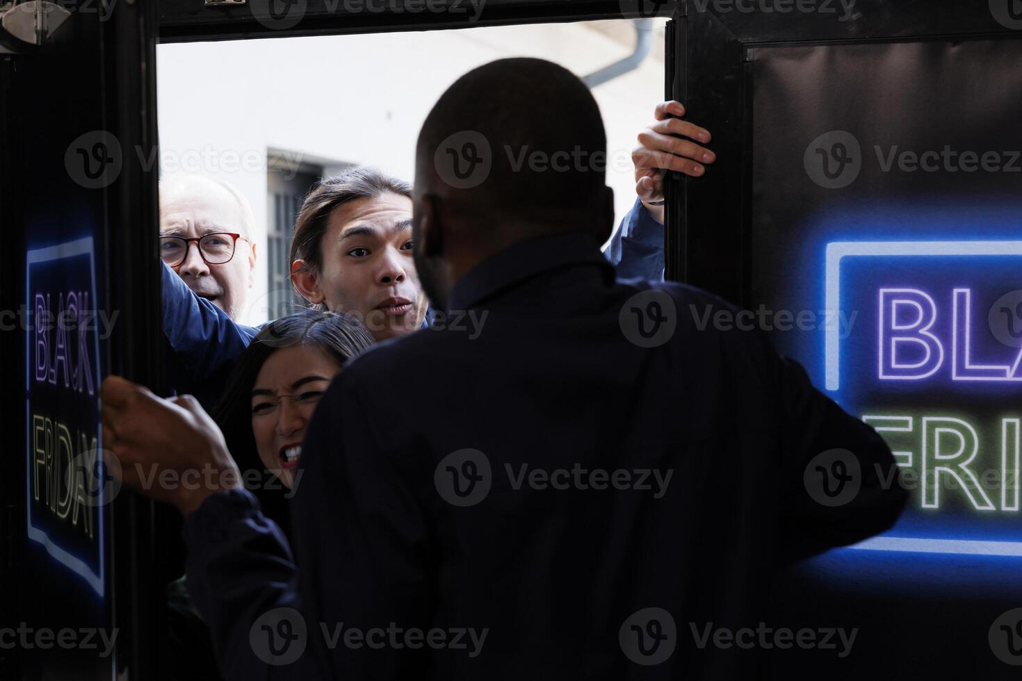 Black Friday madness. Crowd of frenzy diverse customers push security guard and breaking into shopping mall, bargan hunters going crazy to get to retail store first in order to get best deals photo