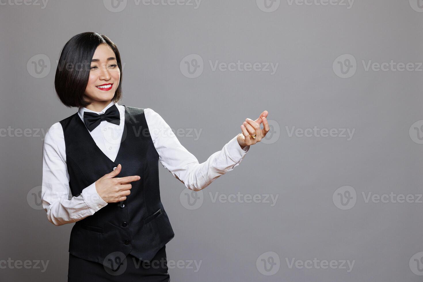 Smiling asian waitress wearing uniform pretending to play guitar while having fun and relaxing. Cheerful woman receptionist imagining to hold musical instrument and expressing happiness photo