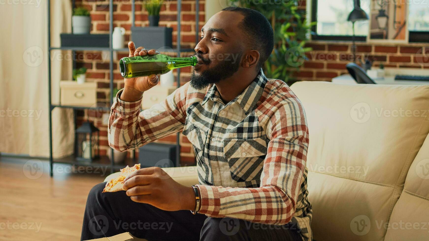 joven hombre comiendo rebanada de Pizza a televisión en sofá, disfrutando eliminar comida y botella de cerveza a hogar. moderno persona servicio para llevar cena y alcohol, acecho película en televisor. foto