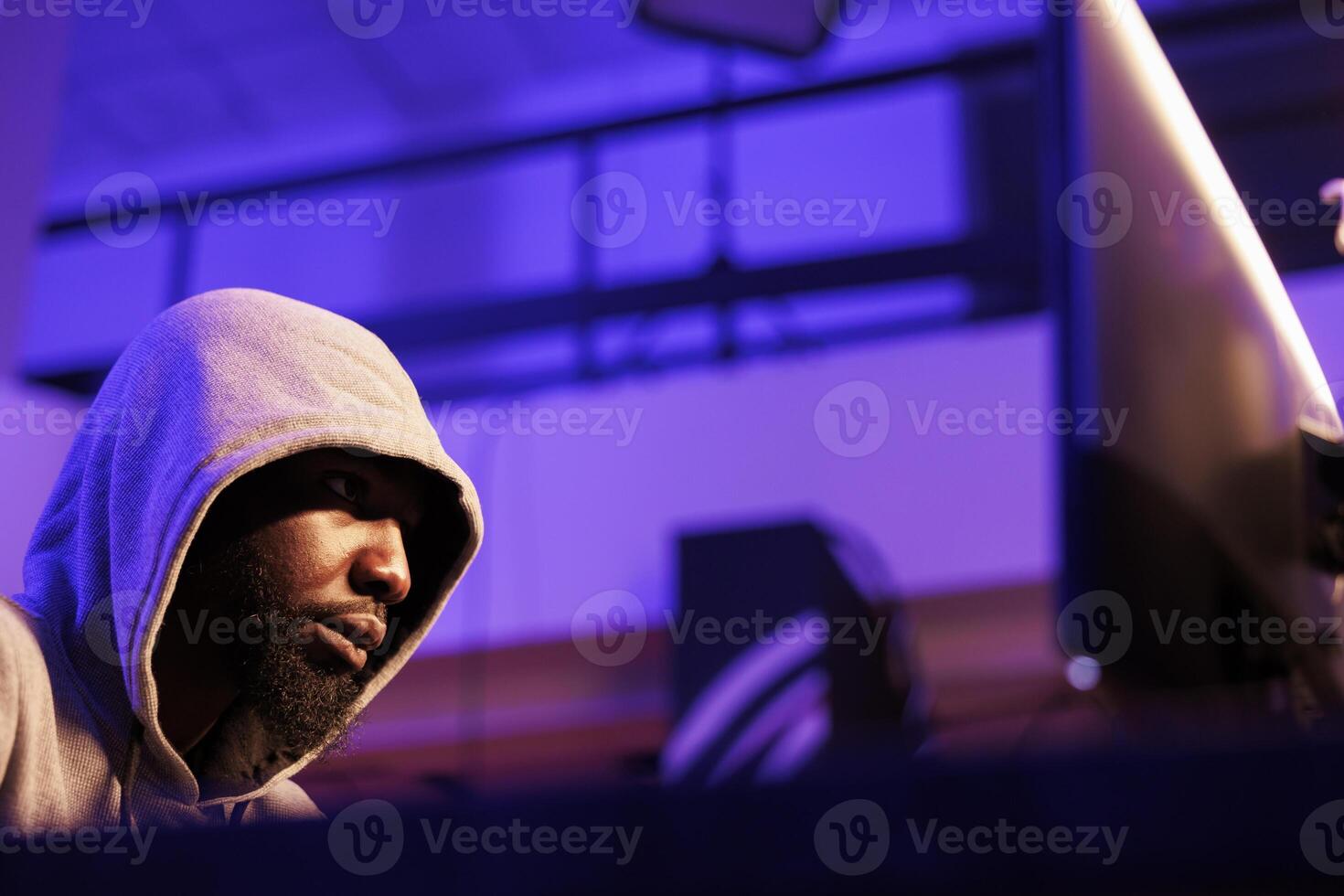 Internet criminal in hood cracking password to break into online server. African american hacker using malicious software to steal database information in abandoned warehouse at night photo