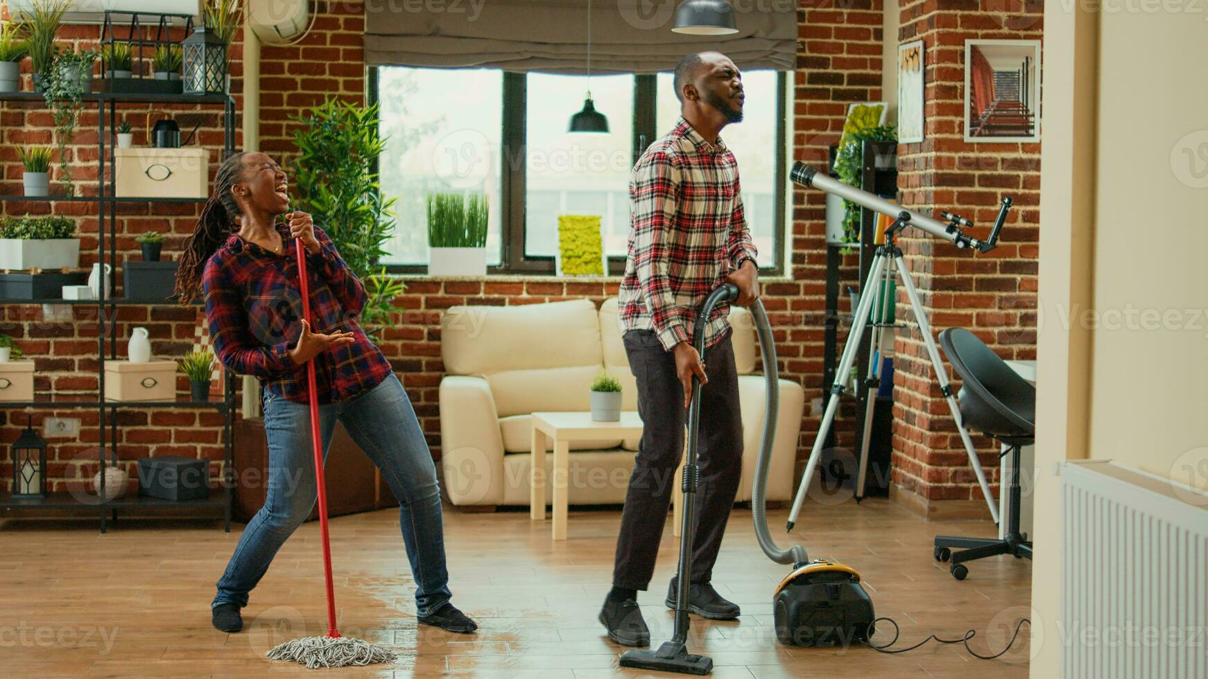 African american partners listening to music and washing floors in living room, doing silly funny dance moves. Cheerful people doing spring cleaning and dancing in apartment, mopping. photo