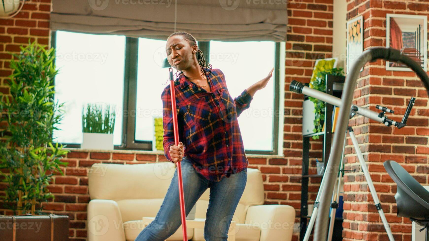Female adult dancing and having fun cleaning household, listening to music and doing dance moves in living room. Modern housewife enjoying washing wooden floors with mop. Handheld shot. photo