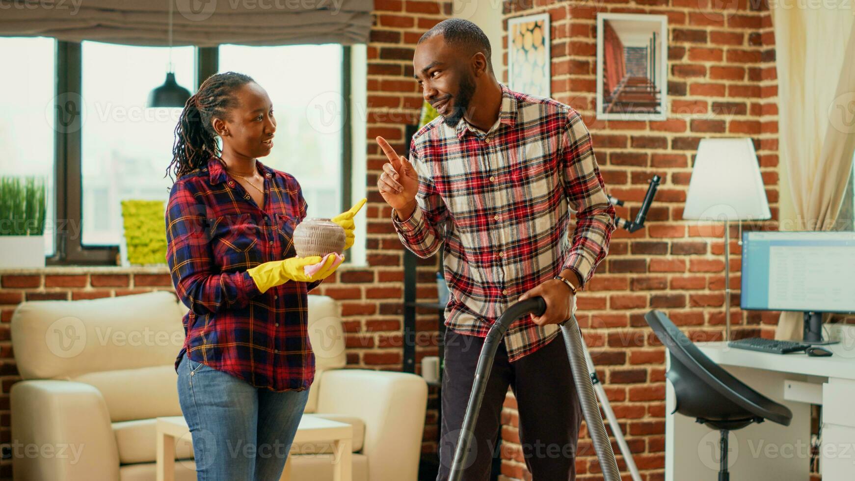 Life partners doing spring cleaning together in living room, focused people doing household chores. Man vacuuming floors and woman sweeping dust off of furniture on shelves, housework. photo