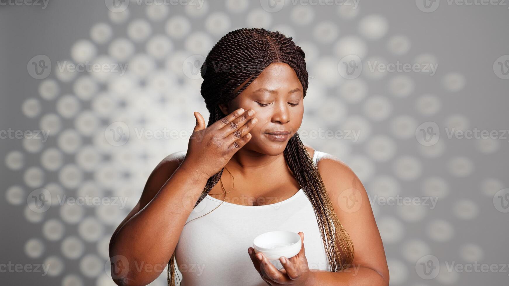 Young person applying moisturizing cream in studio, advertising new skincare cosmetics. Beautiful girl using moisturizer or serum in studio, natural dermatology ad campaign. photo