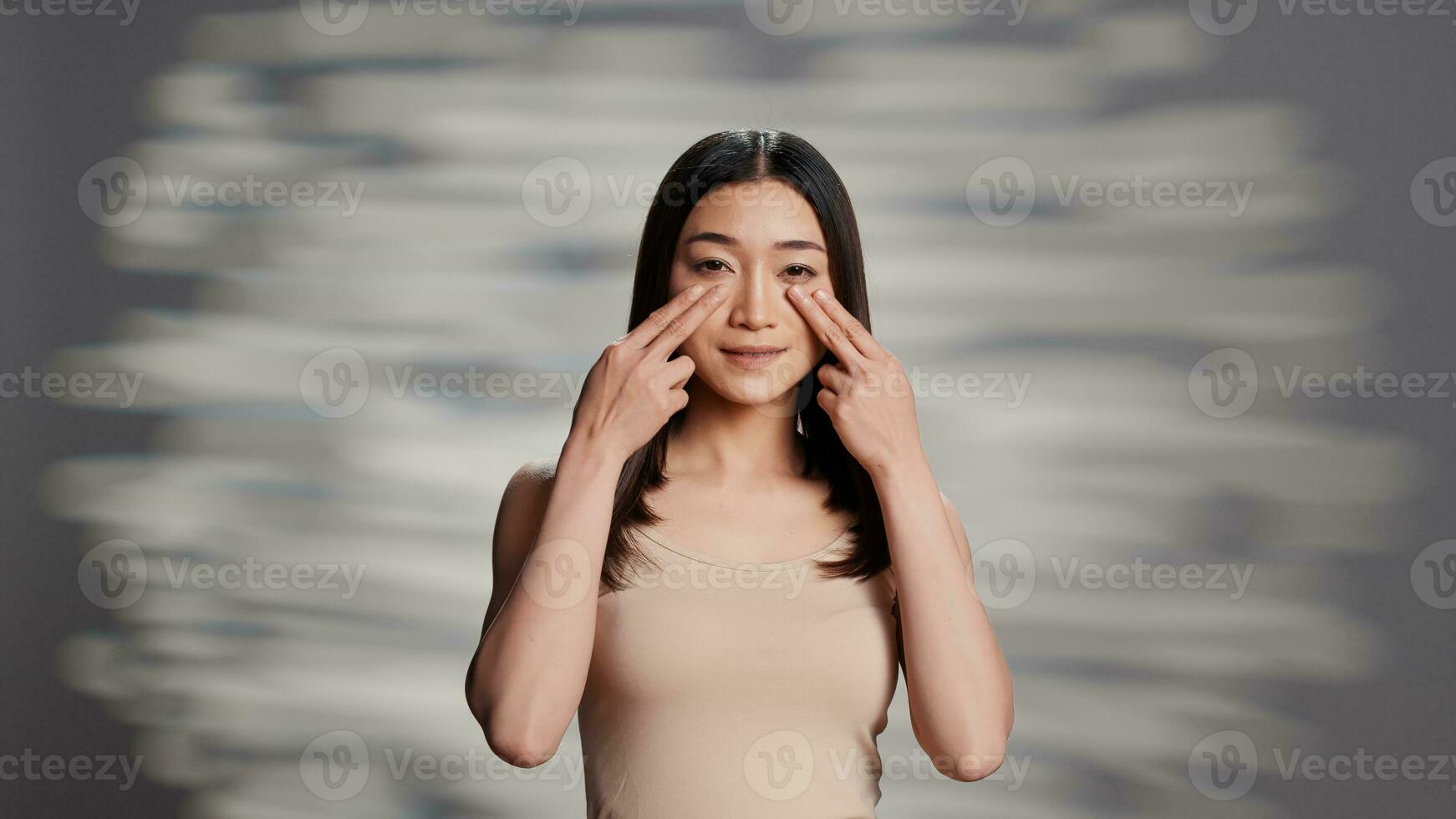 Asian model using moisturizing cream on bare skin, creating bodycare ad campaign for cosmetics. Beautiful gentle girl promoting beauty routine products, apply facial serum on camera. photo