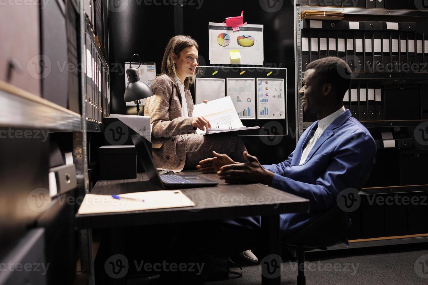 Diverse bookkeepers analyzing management files, working late at night at accountancy report in arhive room. Managers checking bureaucracy record, reading administrative documents photo