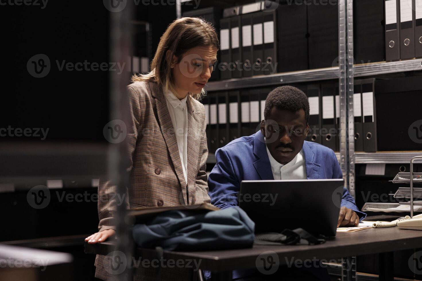 Diverse bookkeepers analyzing accountancy report, checking administrative documents in corporate repository. Storage room employees working late at night reading bureaucracy record photo