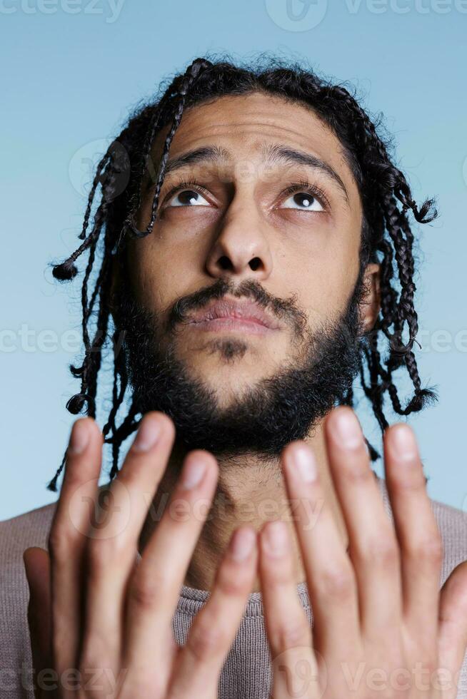 Arab man praying face with hopeful expression and open hands while looking upwards. Young arabian prayer begging, holding palms up and pleading god for forgiveness concept photo