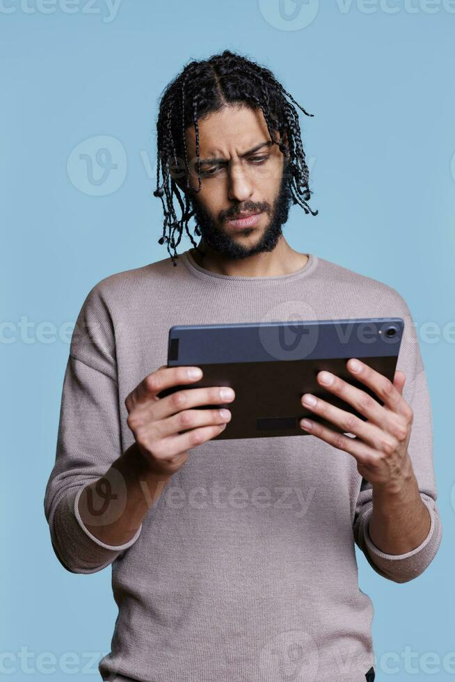 Confused man using digital tablet application and reading news in social media network. Person with concentrated facial expression browsing software app on portable electronic device photo