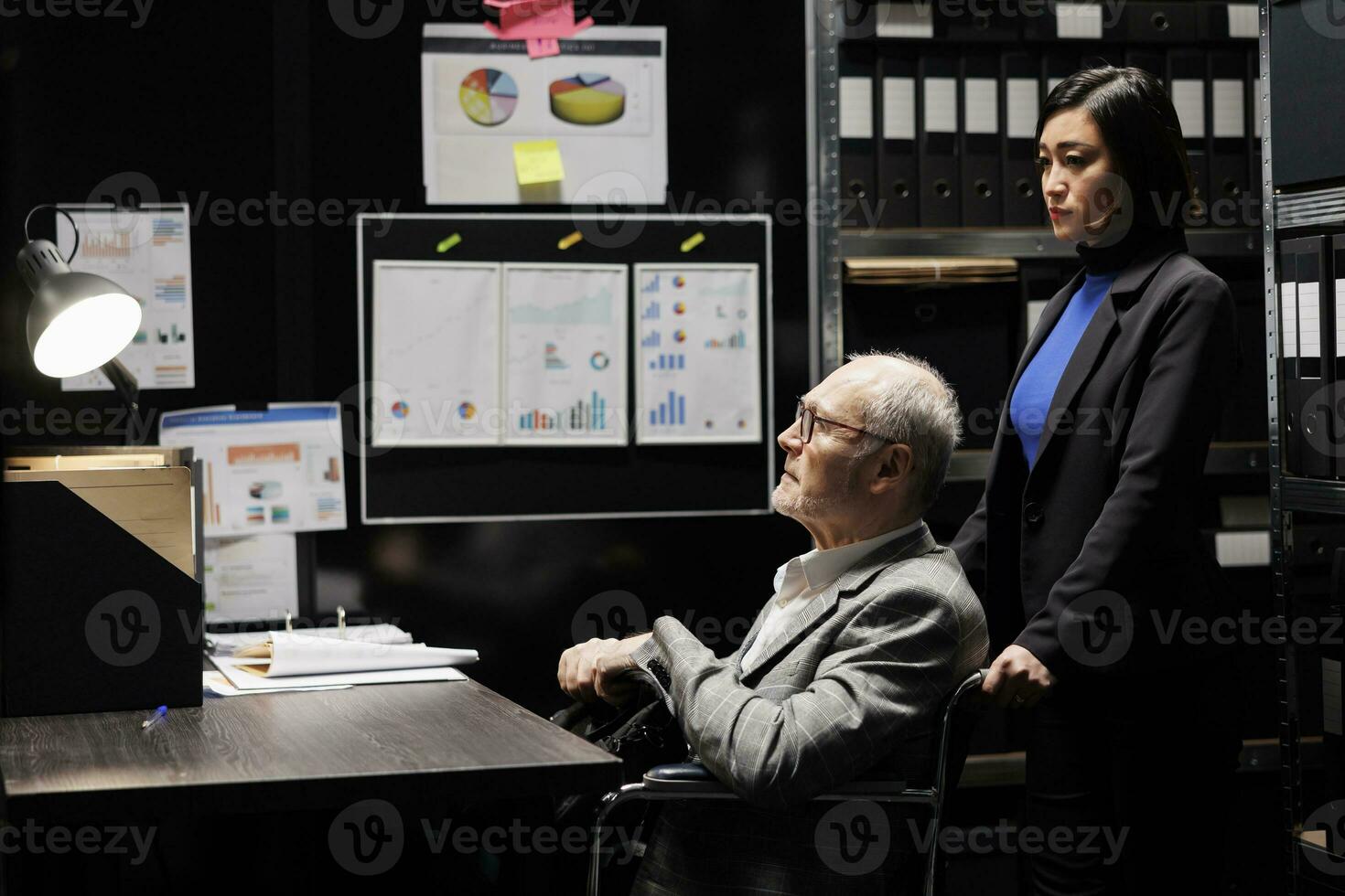 Bookkeeping businessman with disability in wheelchair and coworker working in administrative file room office surrounded by flowcharts. Consultancy bureaucratic workplace filled with business folders photo