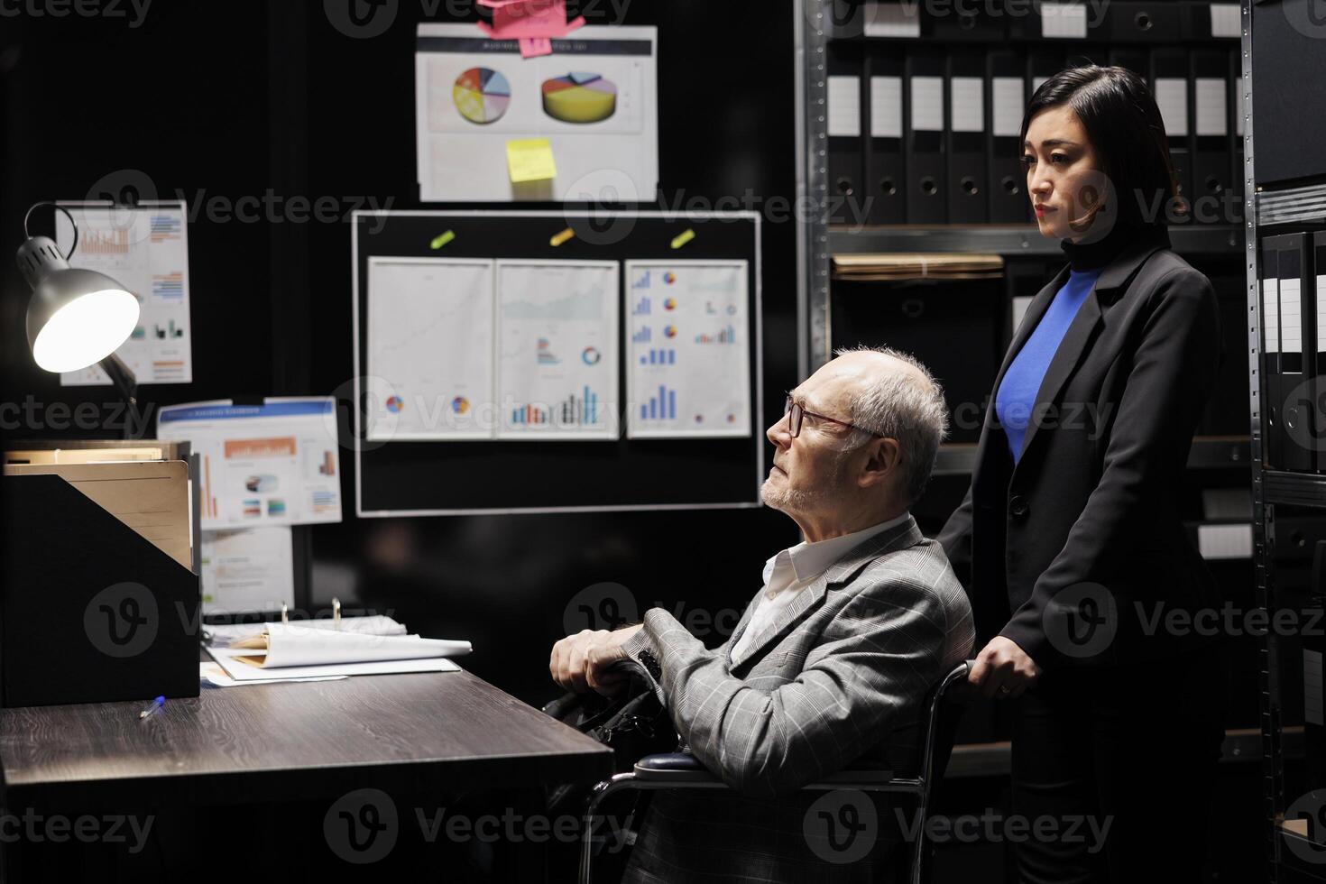 Bookkeeping businessman with disability in wheelchair and coworker working in administrative file room office surrounded by flowcharts. Consultancy bureaucratic workplace filled with business folders photo