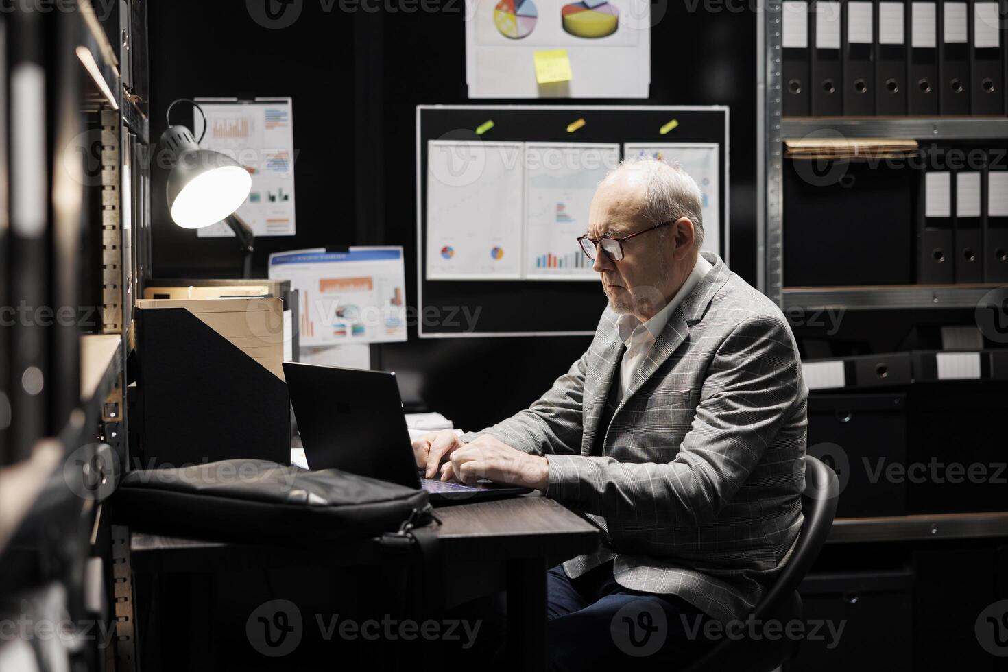 Overworked senior businessman imputing administrative analytical data on laptop. Bookkeeping employee in business accountancy company file cabinet repository surrounded by flowcharts and folders photo