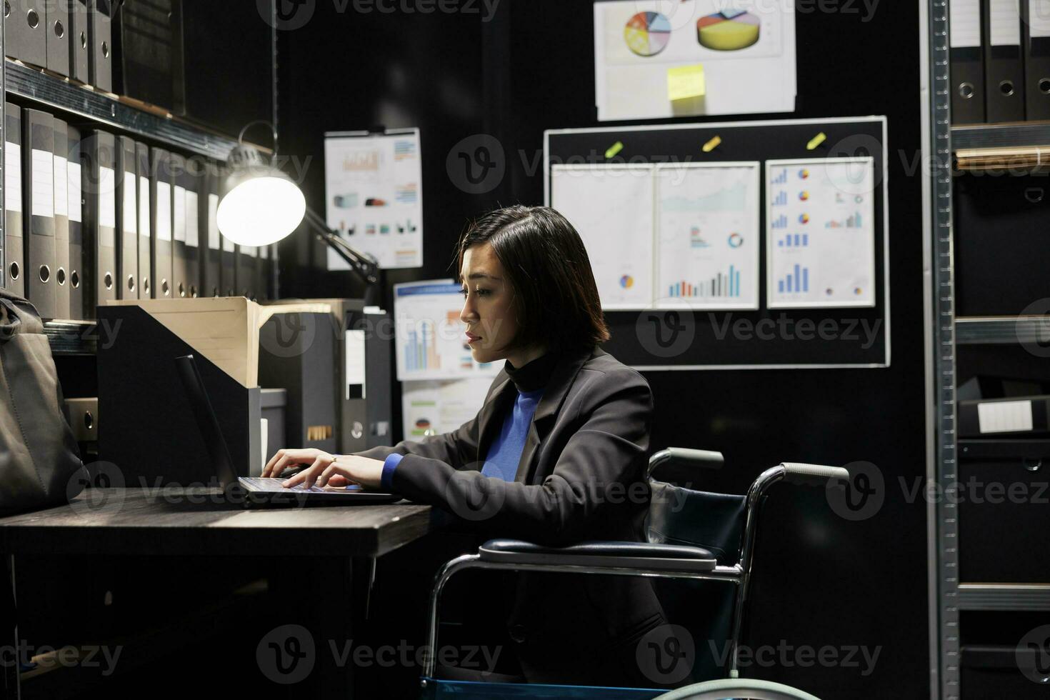 Professional administration businesswoman in wheelchair inserting bookkeeping administrative data paperwork on laptop. Accountancy file cabinet room office filled with folders and diagrams photo