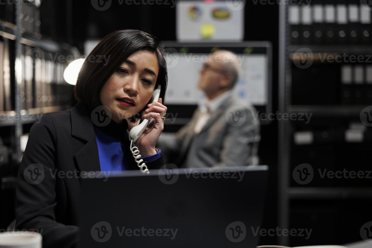 Bookkeeping businesswoman offering consultancy during phone call in administrative workplace. Asian employee in archival depository filled with document folders and flowcharts photo