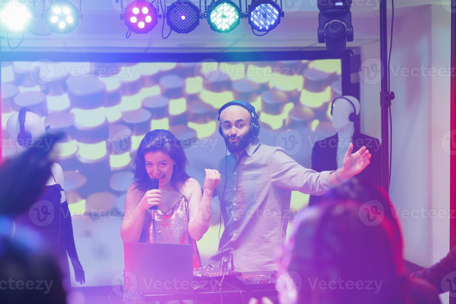 Musicians on stage engaging people to party while performing at nightclub concert. Dj and singer speaking in microphone and entertaining crowd dancing on dancefloor in club photo