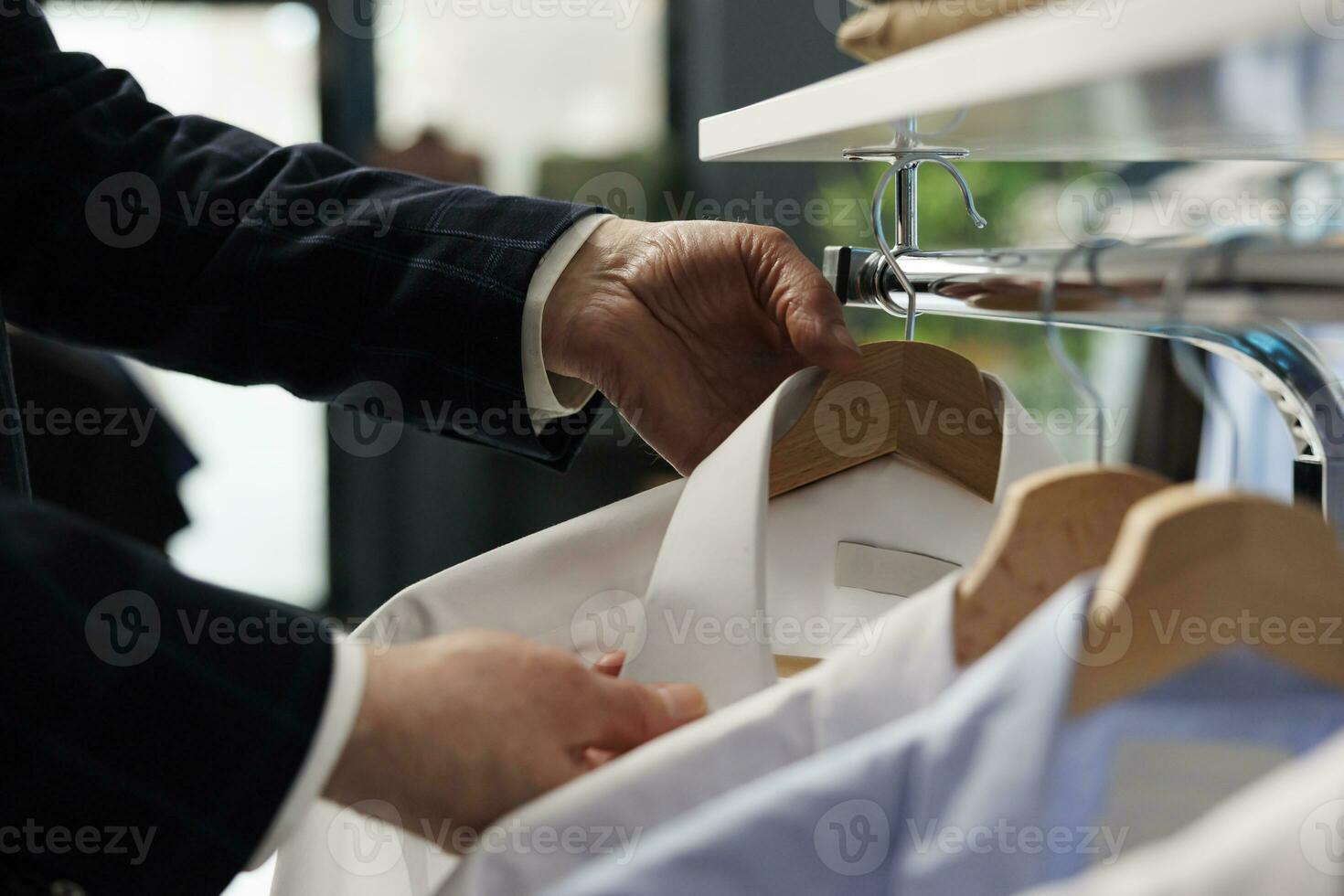 Caucasian man looking at hangers filled with merchandise in showroom, shopping for fashionable clothes. Senior customer buying casual wear to increase wardrobe in clothing store. Close up photo