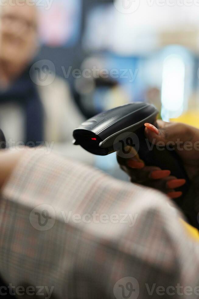 African american employee scanning elegant blouse using store scanner, preparing purchase for senior shopaholic woman. Customer buying stylish wear in clothing store, commercial activity. Close up photo