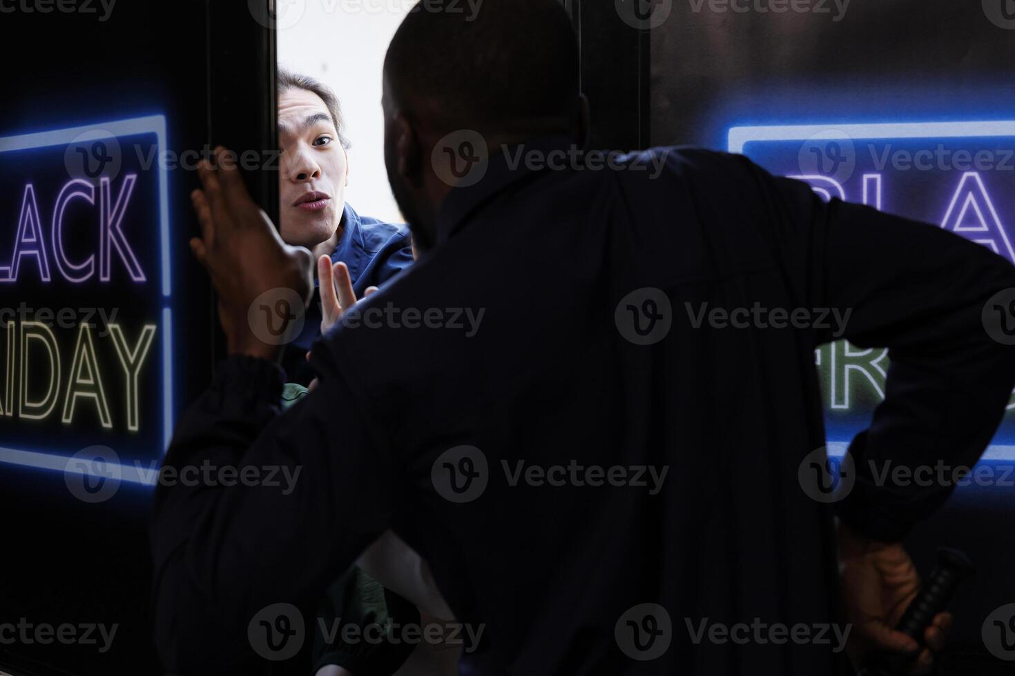 Young Asian guy trying to get inside of retail store on Black Friday before opening hours, crazy shopper fighting and arguing with security guard while standing at shopping mall entrance photo