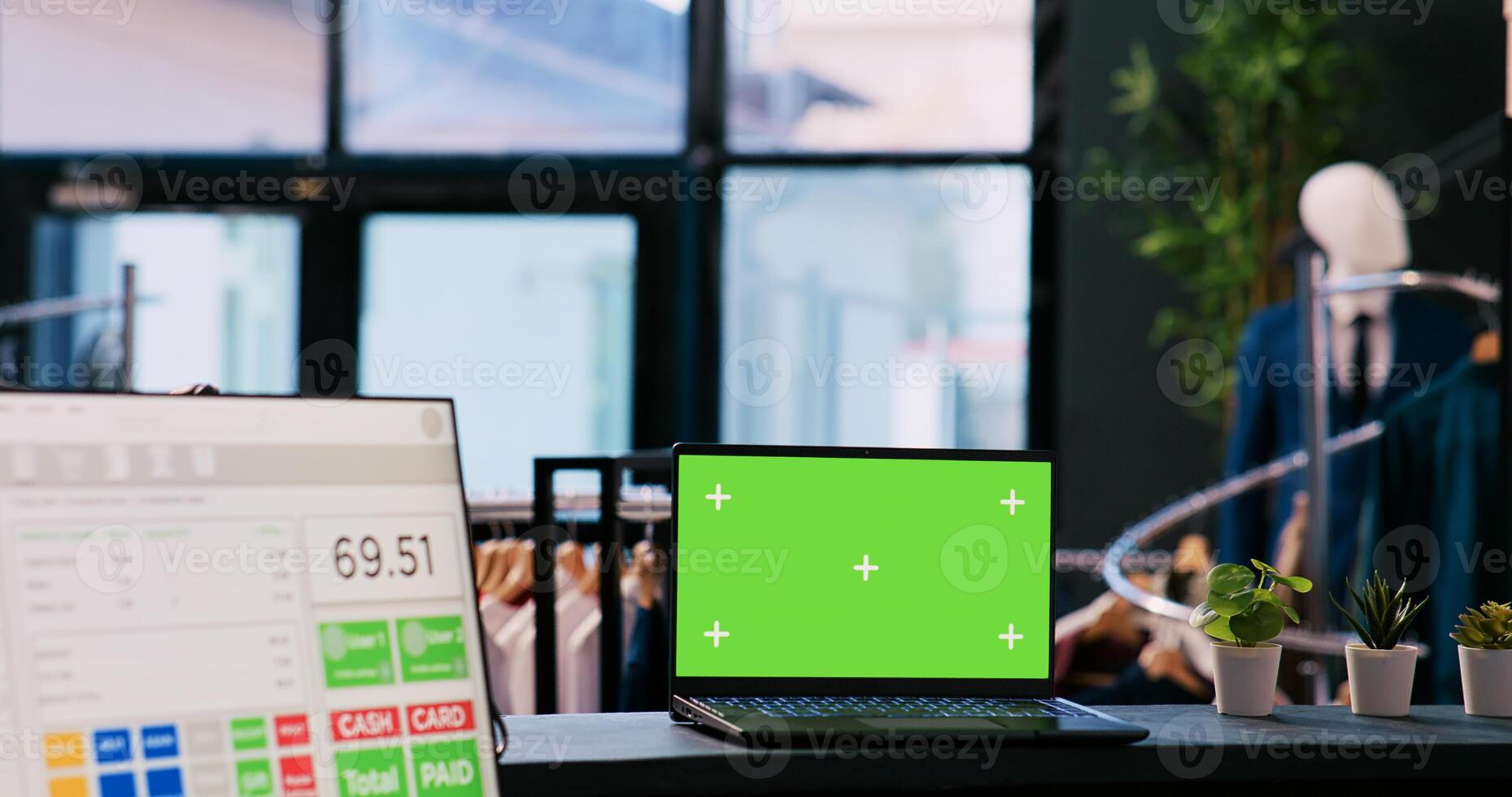 Laptop computer with chroma key green screen mock up display standing on counter desk in modern boutique. In background diverse customers shopping for stylish merchandise in shopping centre photo