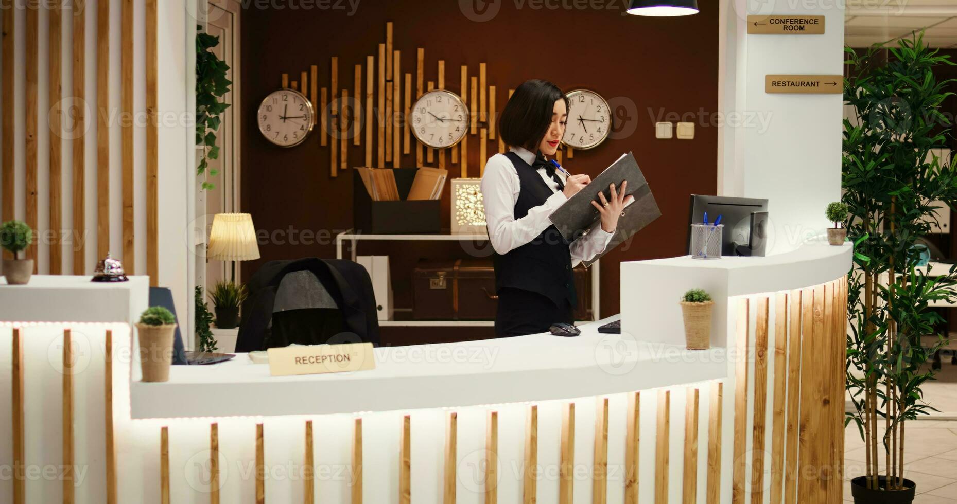 Professional hotel personnel doing administrative tasks in stylish lounge ready to welcome guest. Tourist being helped with luggage by bellhop employee while coworkers prepare her room photo