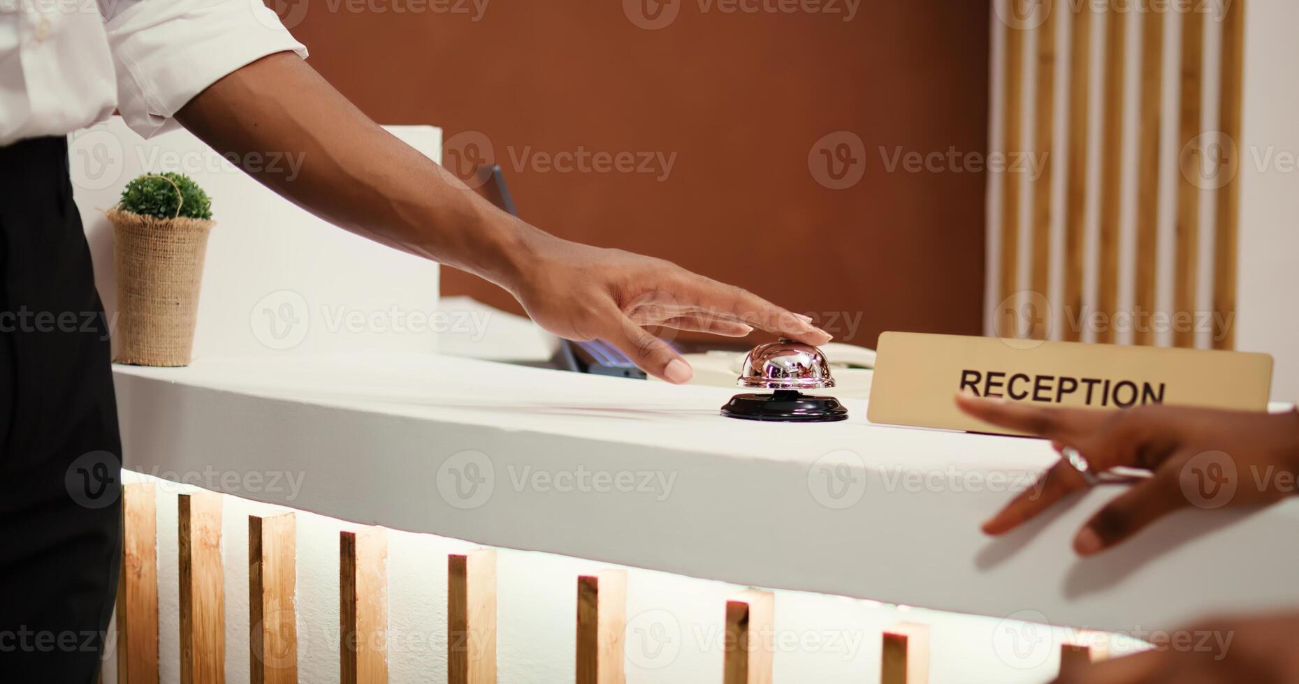 Close up shot of tourists ringing concierge bell at reception front desk, ready to book in their room. Hotel personnel receptionists imputing reservation data during guests check in process photo