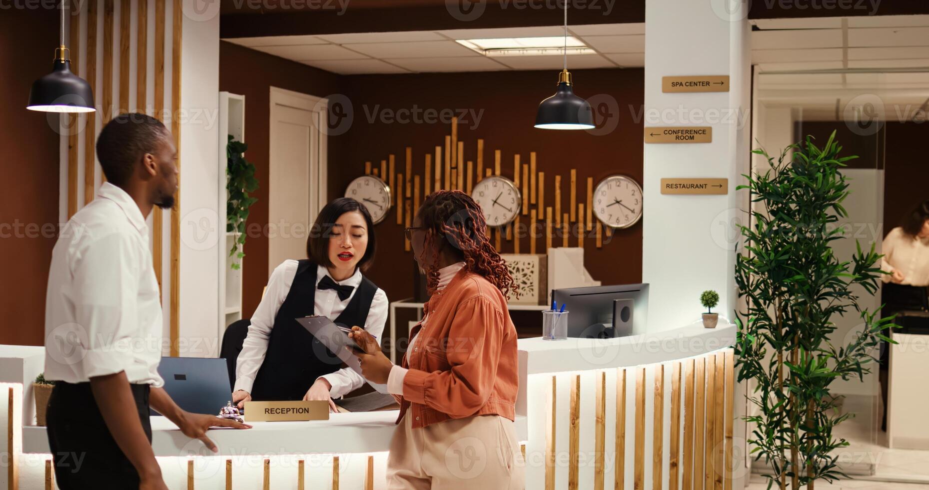 Busy concierge personnel performing various administrative tasks in hotel lobby while guests are being checked in. Tourists booking in their room helped by friendly receptionist and helpful bellboy photo